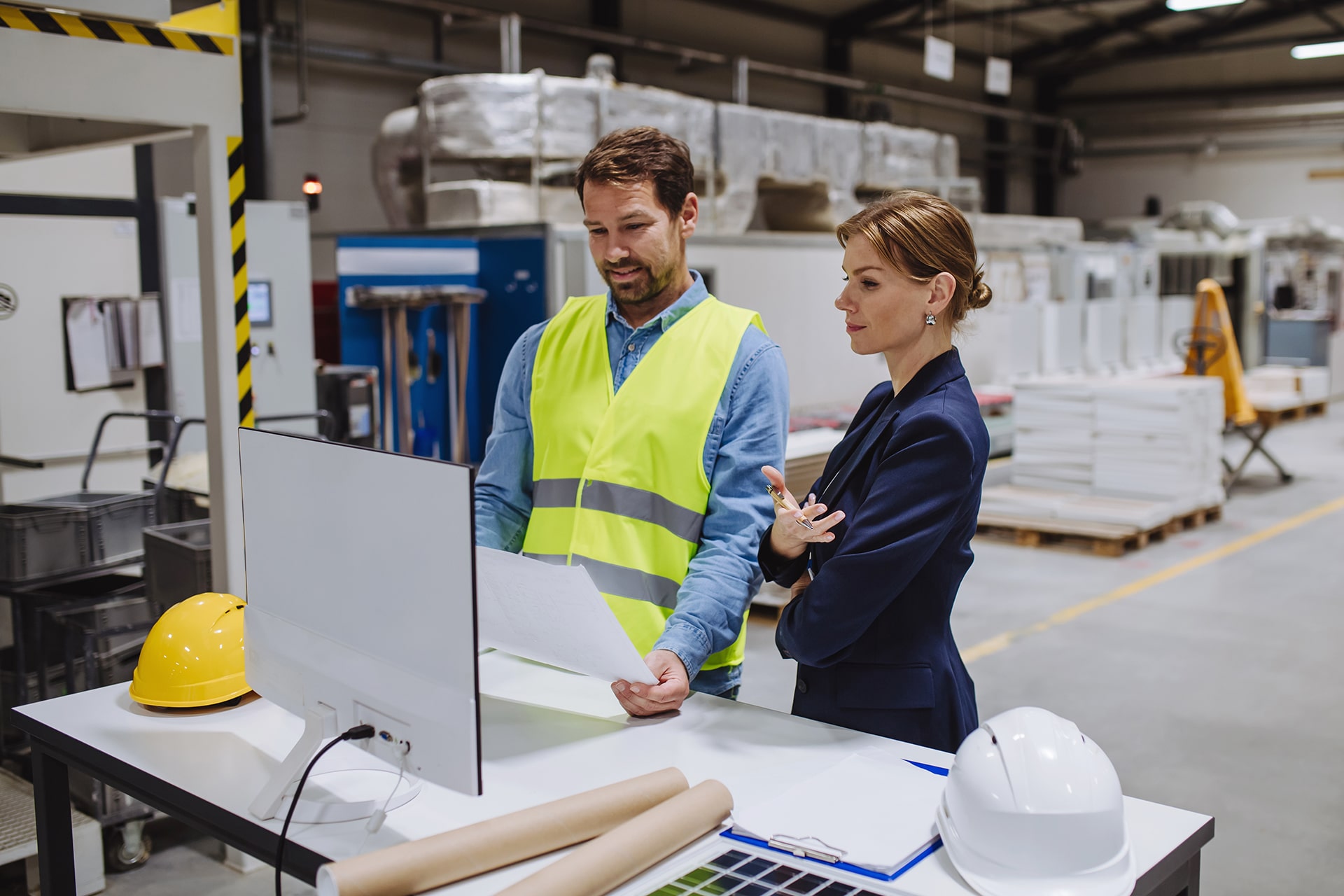 A female engineer is reading technical documentation with the project manager in a modern industrial factory, talking about a new production project or investment.
